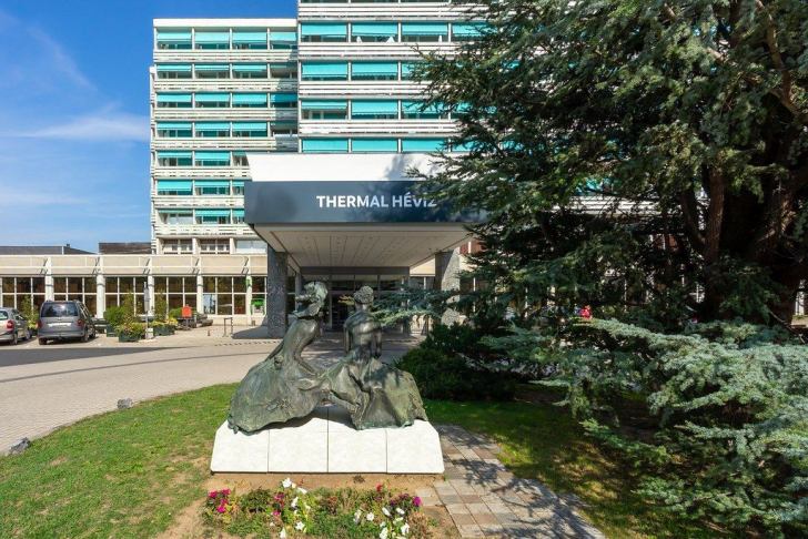 Eine Bronzeskulpturgruppe vor dem großen, modernen Gebäude des Thermal Hévíz.