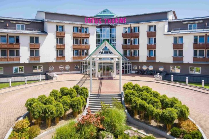 Ein großes, modernes Hotelgebäude namens Lotus Therme mit einem Eingangsbereich und einer gepflegten Außenanlage.